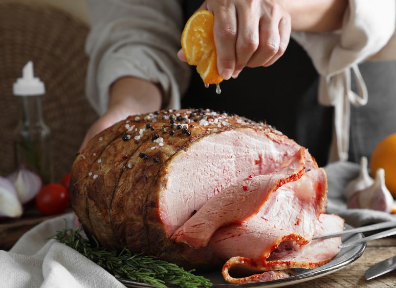 Squeezing orange juice onto glazed ham.