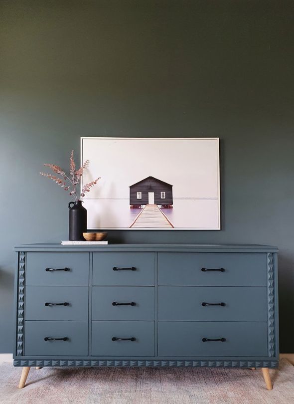 Deep blue dresser with vase and photograph on top.